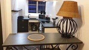A small kitchenette with a microwave, toaster, and sink. There's a table with a woven placemat and a modern lamp.