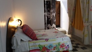 A bedroom with a bed, a wall-mounted light, a poster, and a window with curtains.