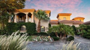 A Mediterranean-style house with a driveway, bicycles, and lush landscaping.