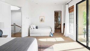 A modern bedroom with a white bed, a small sofa, a framed picture on the wall, and a sliding glass door leading to a balcony.