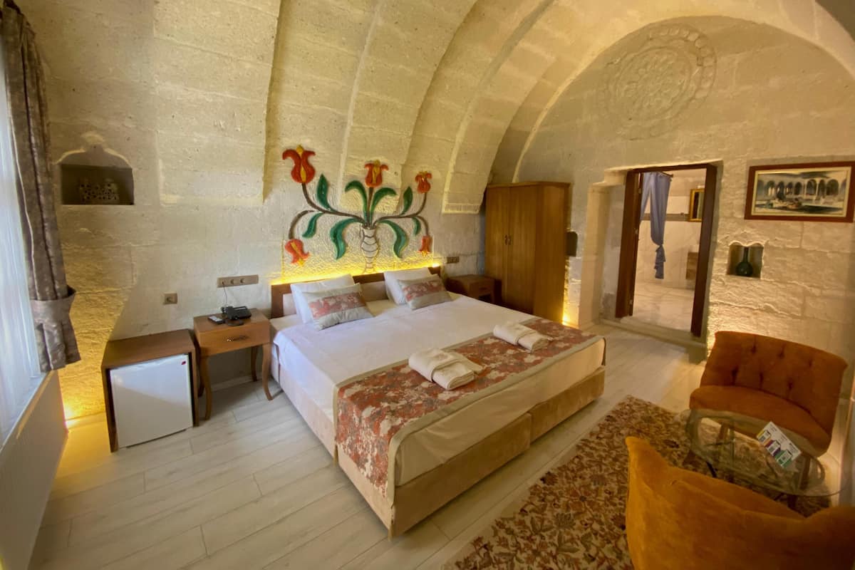 A bedroom with a large bed, a wooden wardrobe, a nightstand, a small table, and a chair.