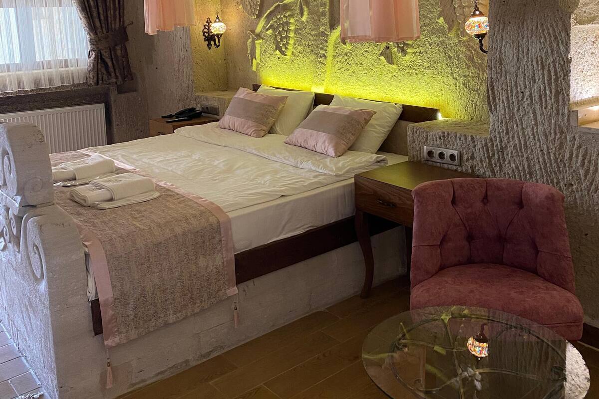 A bedroom with a bed, pillows, a glass table, and a chair.