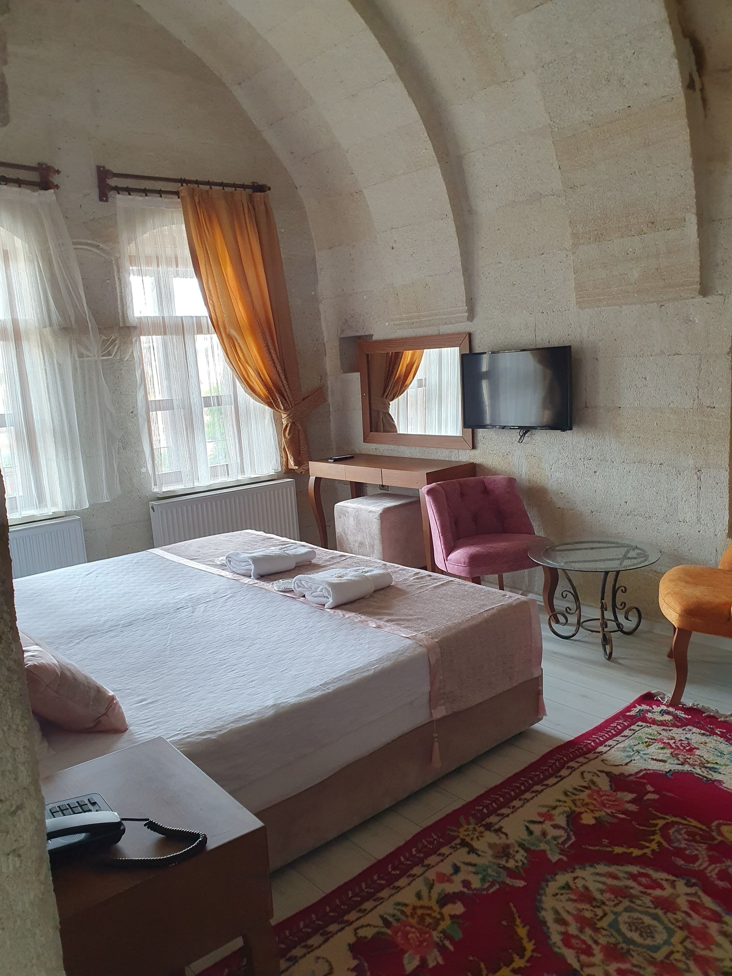 A hotel room with a large bed, a desk, a chair, a TV, and a window with curtains.