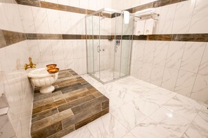 Un baño con piso de mármol, cabina de ducha y lavamanos con lavabo dorado.