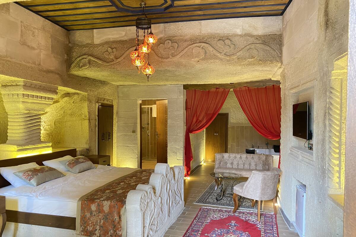 A bedroom with a large bed, a sofa, a TV, and a red curtain.