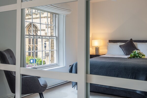 A modern hotel room with a large window, a bed with a dark headboard, and a bedside table with a lamp. - Crown Street, Bury St Edmunds, Suffolk (Bury St Edmunds)