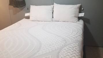 A bed with a white quilt and two pillows, a white dress on a mannequin, and a grey wall.