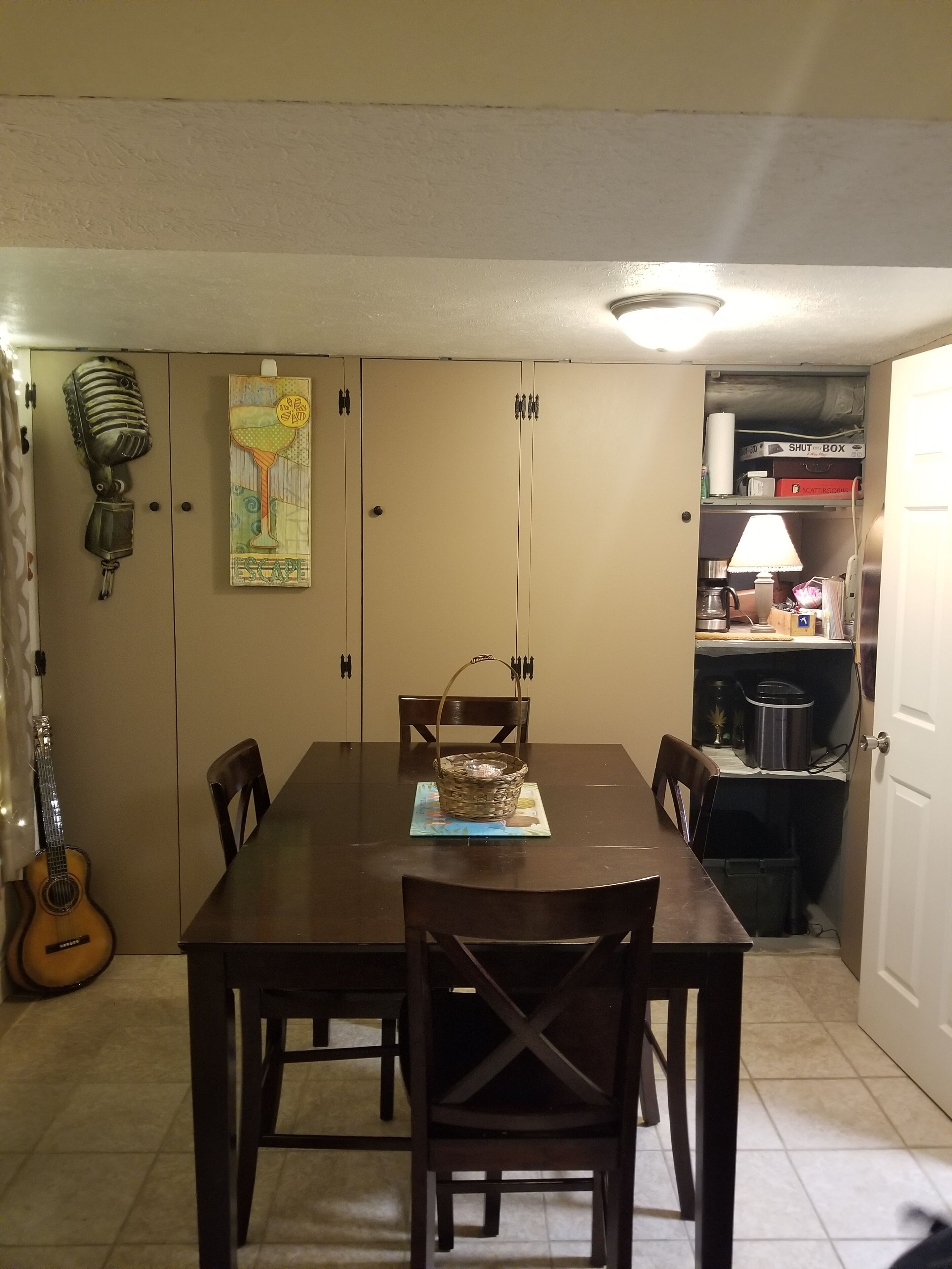 Un coin repas avec une table en bois, des chaises, une guitare et un mur orné d’une affiche.
