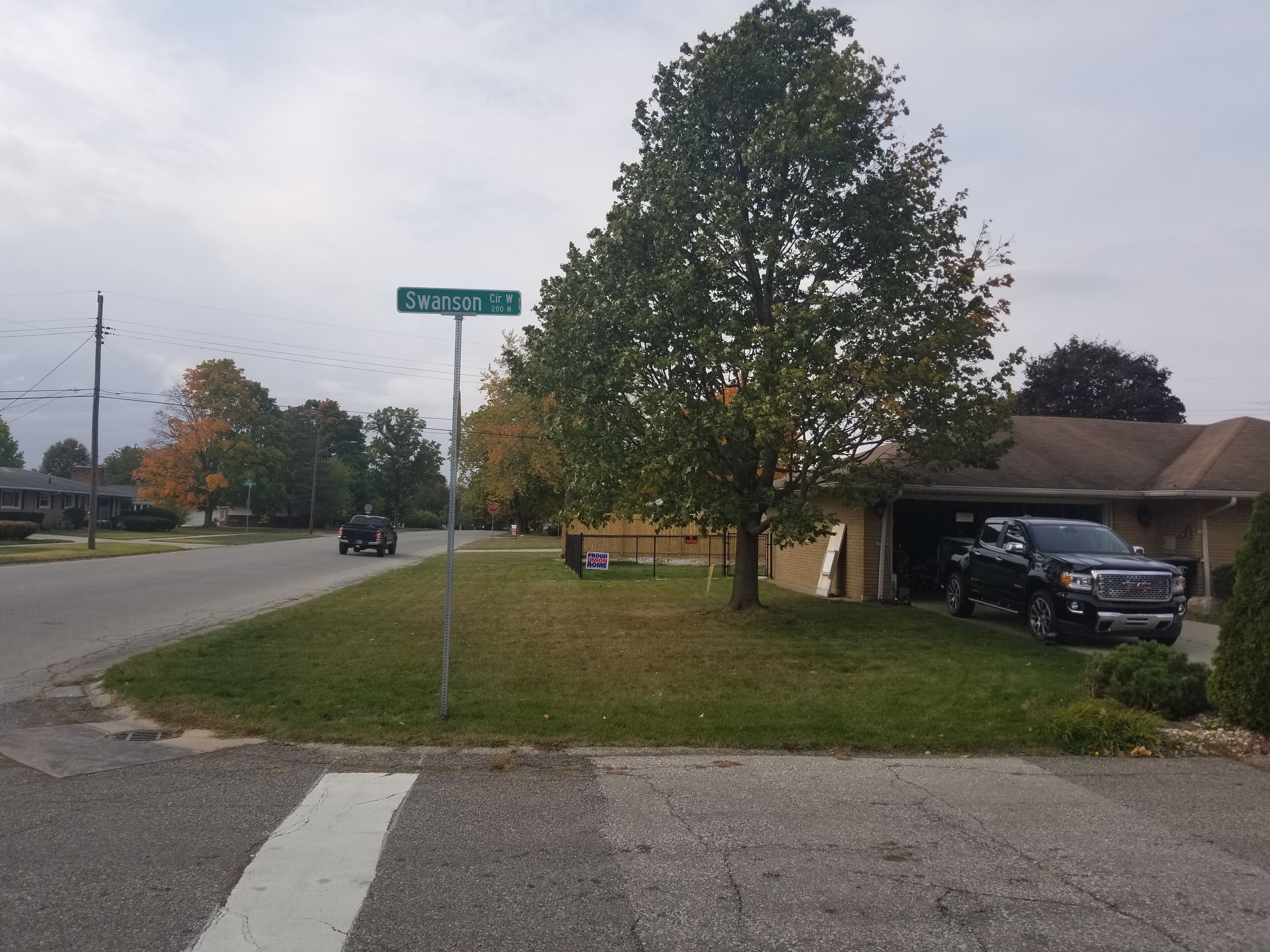 Straßenschild für Swanson Cir W, ein Wohngebiet mit Häusern, einer Einfahrt und einem parkenden Lastwagen.
