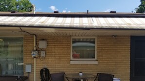 Un patio con dos sillas de mimbre y una mesita, un cubo de basura y una ventana con un cartel que dice 'Posted No Trespassing'.