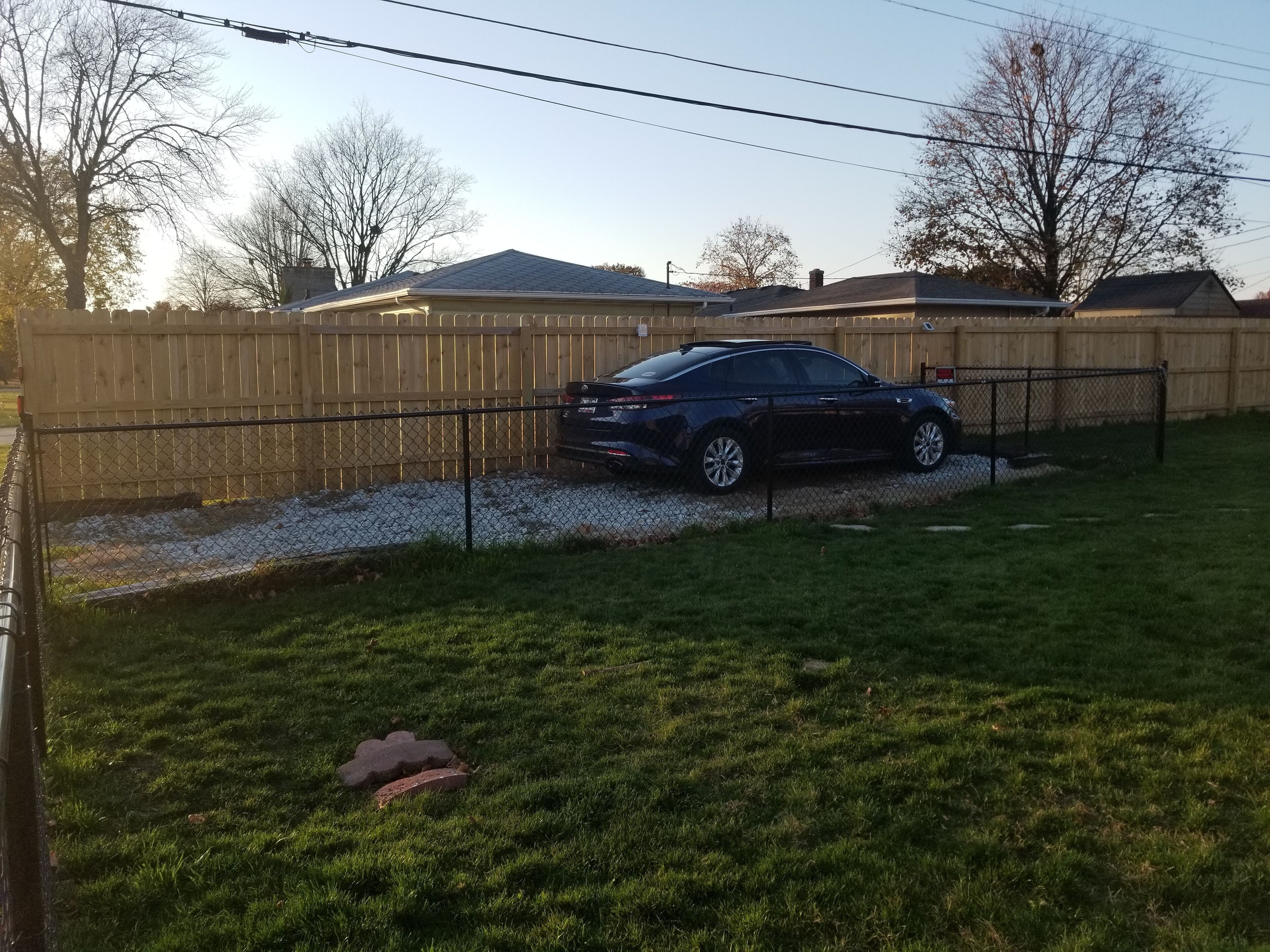 A fenced backyard with a parked car, a wooden fence, and a grassy lawn.