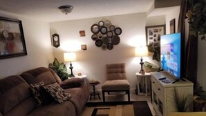 Una sala de estar con un sofá marrón, un sillón amarillo, un televisor y una pared decorada con espejos circulares.