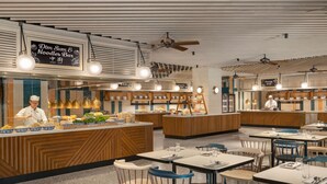 Een modern restaurantinterieur met een centrale balie, een zithoek en een kok die gerechten bereidt.