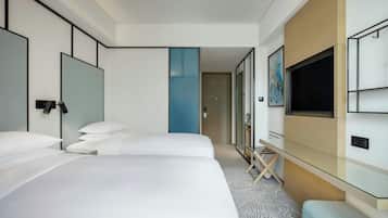 A hotel room with two beds, a TV, a desk, and a large window.