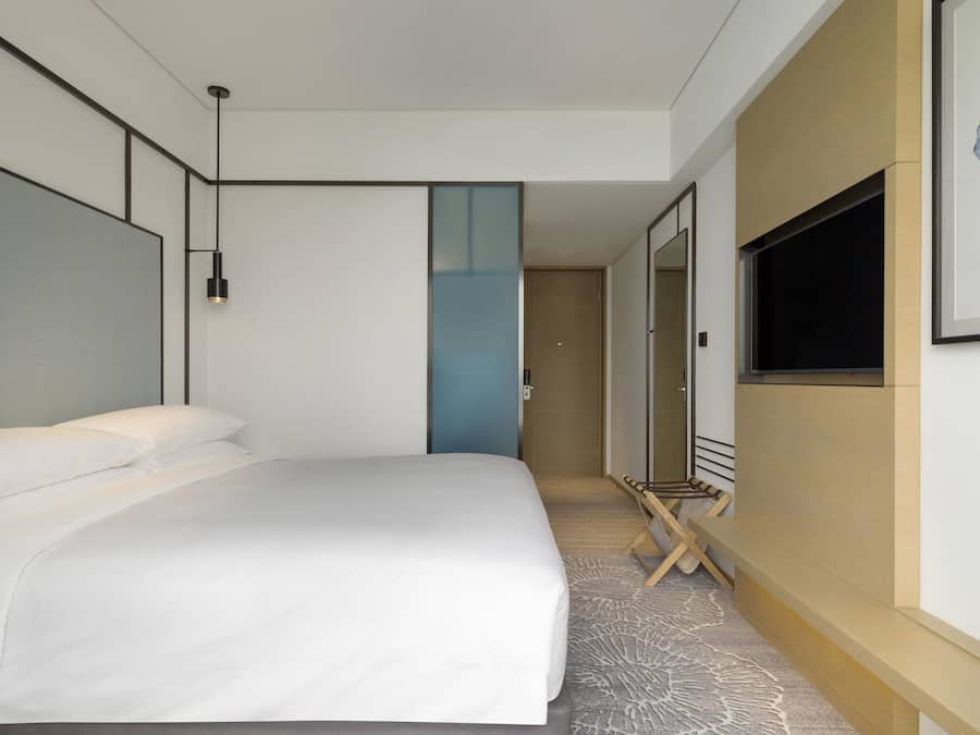 A modern hotel room with a large bed, a flat-screen TV mounted on the wall, and a small seating area with a table and chairs.