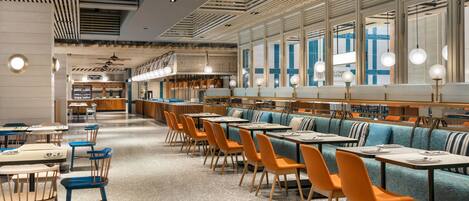 A modern restaurant with high ceilings, wooden paneling, and a mix of blue and orange seating.