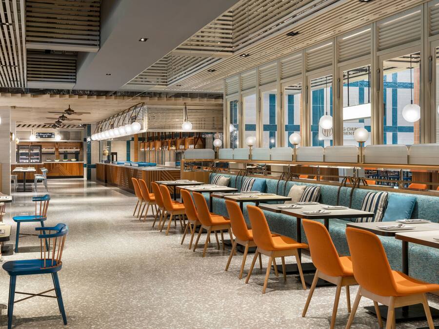 A modern restaurant with high ceilings, wooden paneling, and a mix of blue and orange seating.