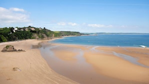 Ein Strand mit sandigem Ufer, ruhigem Wasser und einer entfernten Küstenlinie mit Gebäuden.