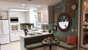 A modern kitchen with white cabinets, a central island, and a dining area with a bench. - Quiet, Stand-alone Country Granny Cottage near the Village, (Arroyo Grande)