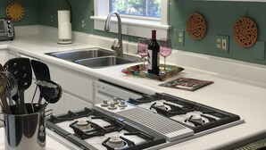 A modern kitchen with white cabinets, a stainless steel sink, a gas stove, and decorative wall plates. - Quiet, Stand-alone Country Granny Cottage near the Village, (Arroyo Grande)