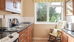 A kitchen with wooden cabinets, a stove, a microwave, and a window with a view of greenery outside.