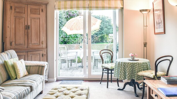 A cozy living room with a sofa, ottoman, and a table with chairs.