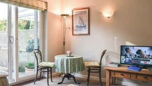 A cozy living room with a television, a table with chairs, a sofa, and a large window with a view of greenery outside.