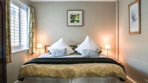 A bedroom with a bed, two bedside lamps, a window with curtains, and two framed pictures on the wall.