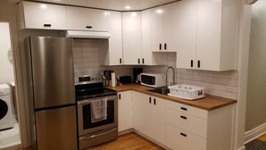 A compact kitchen with white cabinets, stainless steel appliances, and a wooden countertop.