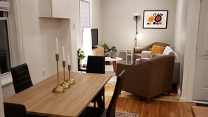 A modern living room with a dining area, white walls, and a wooden floor.