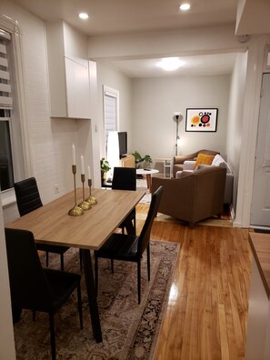 A modern living room with a dining area, white walls, and a wooden floor.