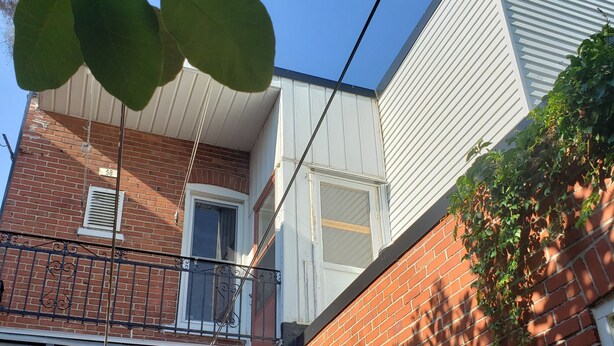 A two-story building with a brick facade, a white upper section, and a balcony with a metal railing.