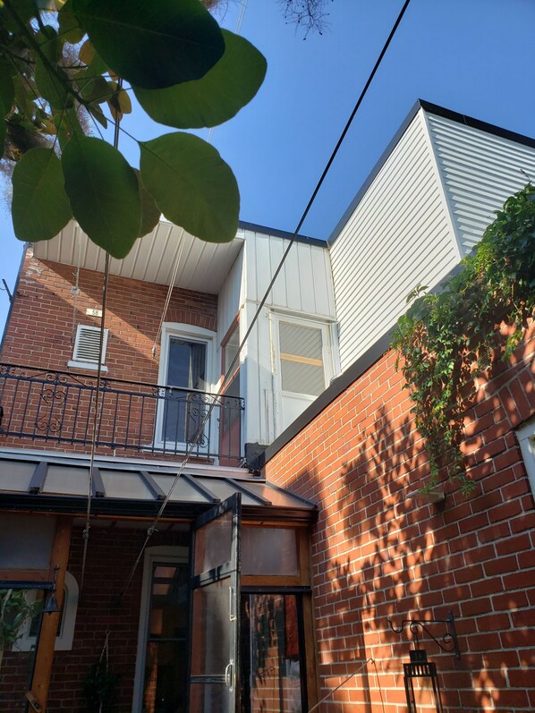 A two-story building with a brick facade, a white upper section, and a balcony with a metal railing.