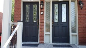 A two-door entrance with a brick facade, a covered porch, and a black mat at the steps.