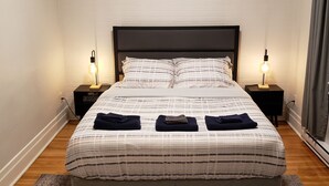 A neatly made bed with a striped bedspread, two bedside tables with lamps, and a patterned rug on a wooden floor.