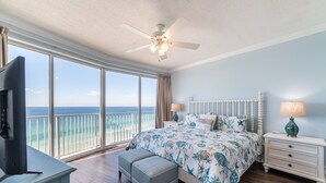 A bedroom with a large bed, a ceiling fan, a TV, and a view of the ocean. - Beachfront 2BR/2BA PCB condo with Gulf views (Panama City Beach)