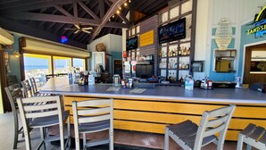 A bar area with a long counter, multiple seating options, and a view of the ocean. - Beachfront 2BR/2BA PCB condo with Gulf views (Panama City Beach)