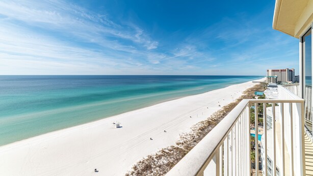 A beach view from a balcony with a clear sky, a sandy beach, and a few buildings in the distance. - Beachfront 2BR/2BA PCB condo with Gulf views (Panama City Beach)