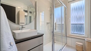 Een moderne badkamer met een douchecabine van glas, een grote spiegel en een witte wasbak.