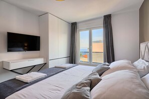 A modern hotel room with a large bed, a flat-screen TV, a wardrobe, and a balcony with a view of the sea. - Apartment Liberty Living with Pool IV (Split)