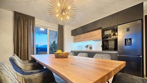 Una cocina moderna con refrigerador empotrado, una mesa de comedor con sillas y un ventanal con cortinas.