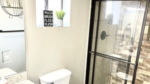 A bathroom with a toilet, a shower with a glass door, a sink with a countertop, and a mirror.