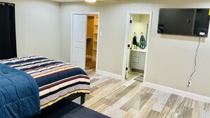 A bedroom with a bed, a ceiling fan, a TV mounted on the wall, and a door leading to a bathroom.