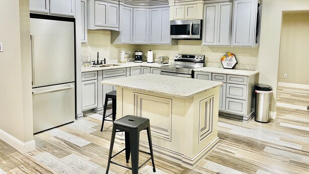 A modern kitchen with grey cabinetry, a central island, stainless steel appliances, and a herringbone-patterned floor.