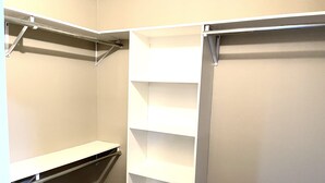 A walk-in closet with white shelving units and a metal rod for hanging items.