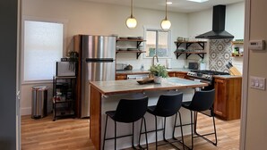 Une cuisine moderne dotée d’un îlot central, de tabourets de bar, d’appareils électroménagers en acier inoxydable et de luminaires suspendus.