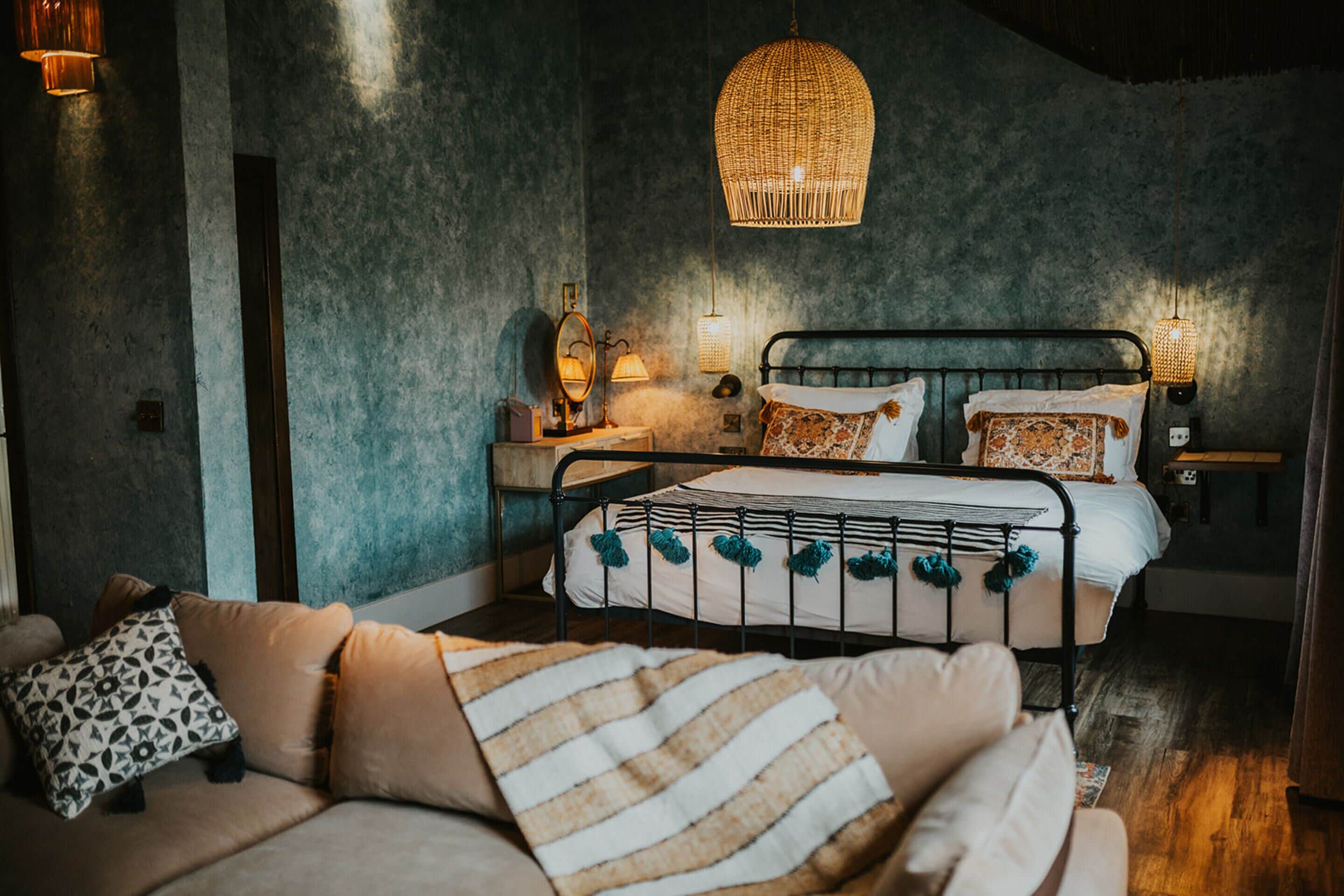 A cozy bedroom with a metal bed frame, a cushioned sofa, and a hanging light fixture.