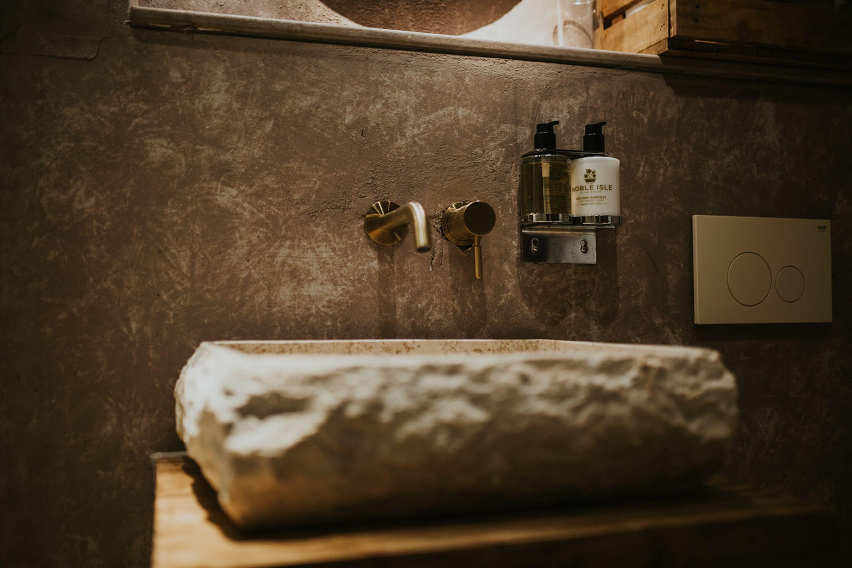 A bathroom with a stone sink, a towel, and a soap dispenser on the wall.
