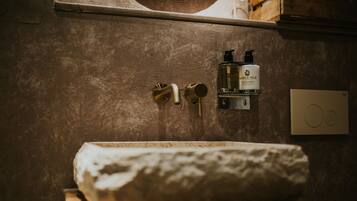 A bathroom with a stone sink, a towel, and a soap dispenser on the wall.