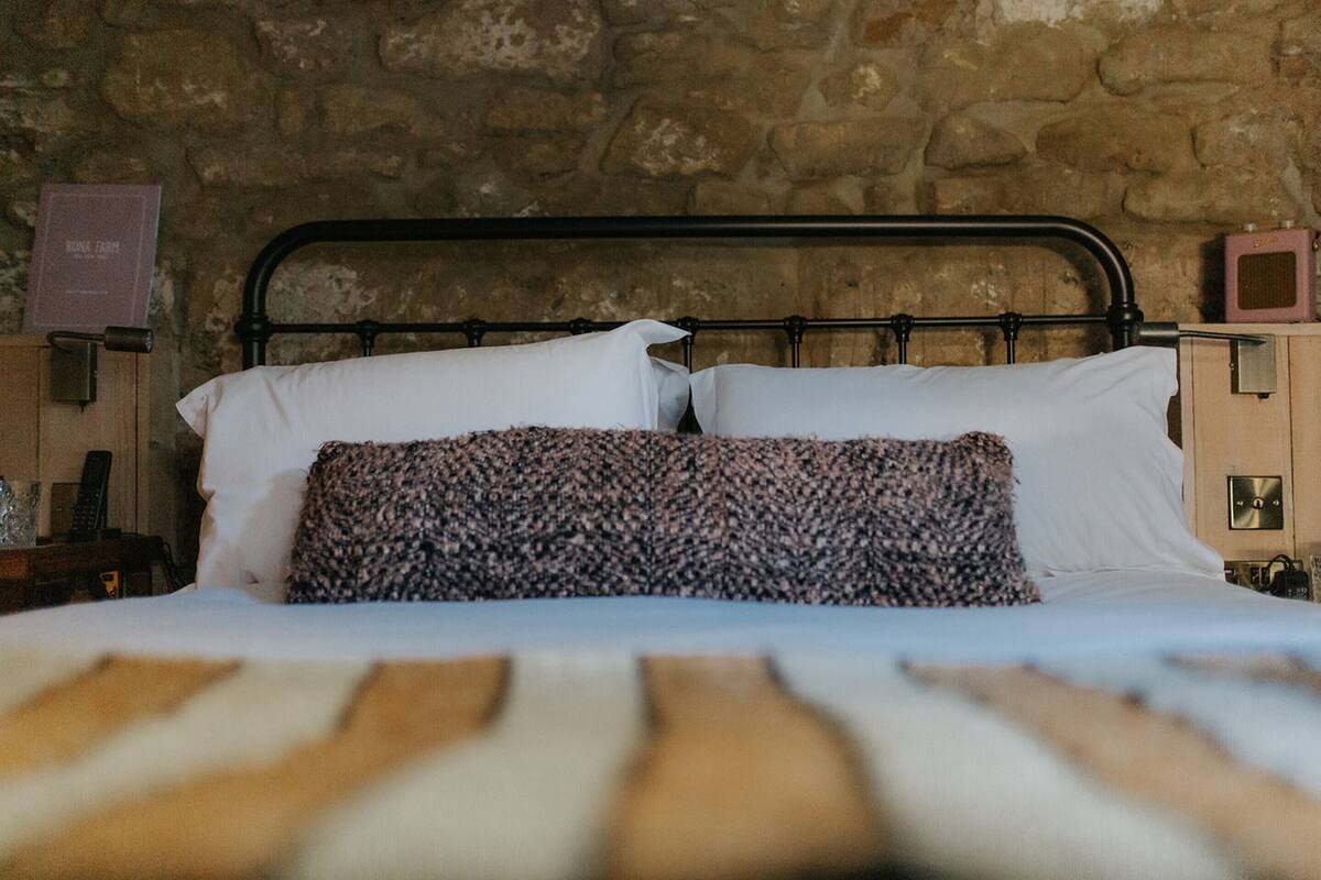A bed with a metal frame, white pillows, and a patterned throw.